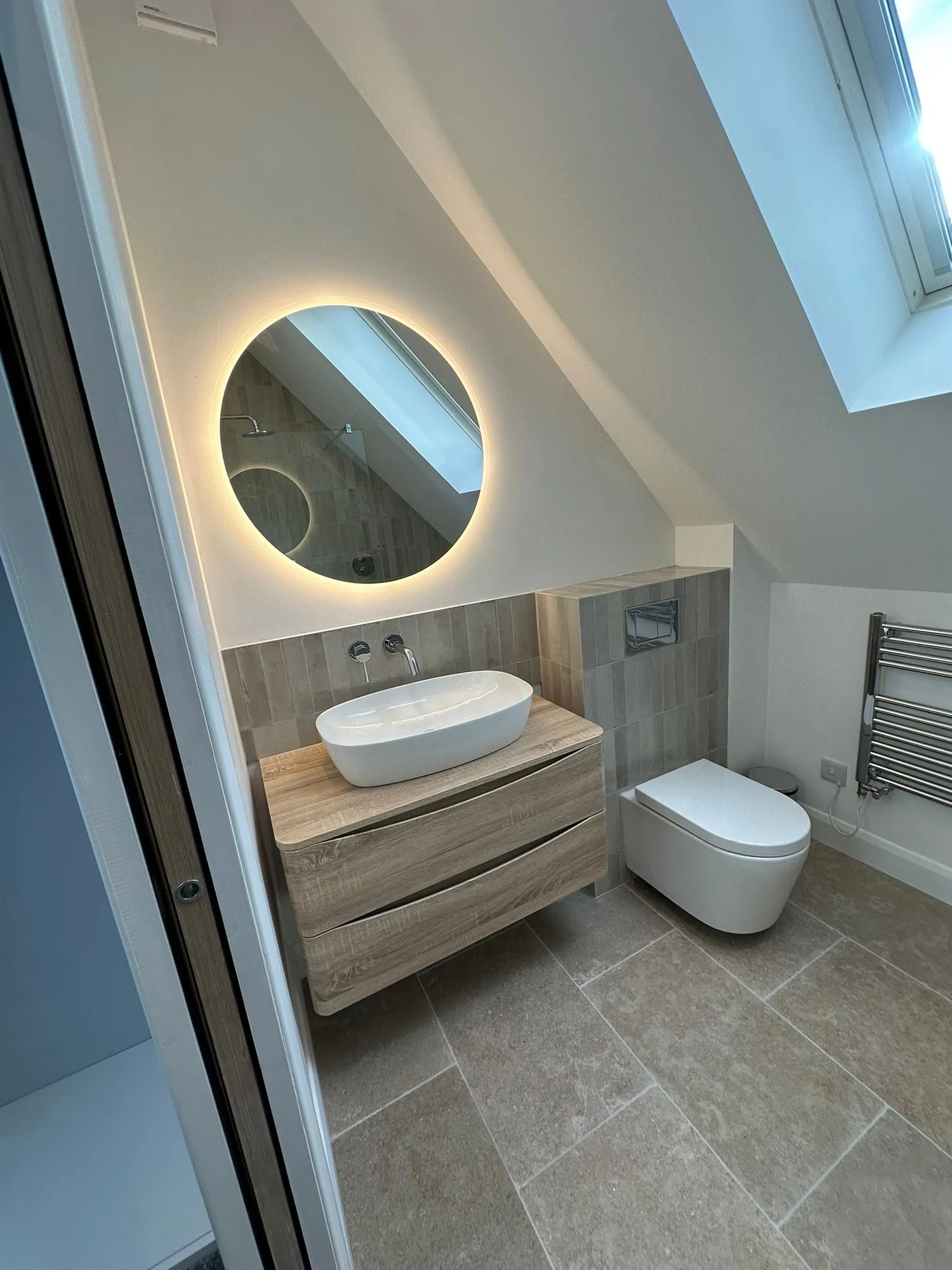 Contemporary loft ensuite with wall-hung vanity, vessel basin and backlit round mirror by HES Plumbing & Electrical
